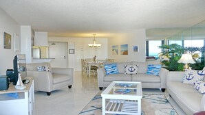 A spacious living room with a beige sofa, a coffee table, and a dining area with a chandelier. - SEA MAR CONDO: 19th Floor Penthouse South Seas Tower 4 With Awesome Views (Marco Island)