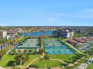 Un quartier résidentiel situé sur la côte, comprenant plusieurs immeubles, un port de plaisance et des courts de tennis.