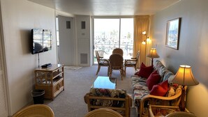 A living room with a television, a sofa, a table, and a balcony with a view of the city. - Ocean View Condo - Ilikai Marina Waikiki Honolulu (Honolulu)