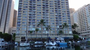 A high-rise building with multiple balconies, a marina with boats, and palm trees. - Ocean View Condo - Ilikai Marina Waikiki Honolulu (Honolulu)