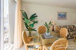 A living room with wicker furniture, a glass table, and large plants.