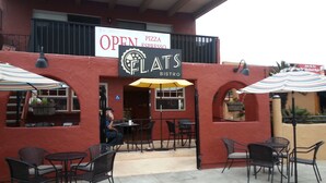An outdoor seating area with tables and chairs, a sign indicating the establishment is open, and a menu board advertising pizza and espresso.