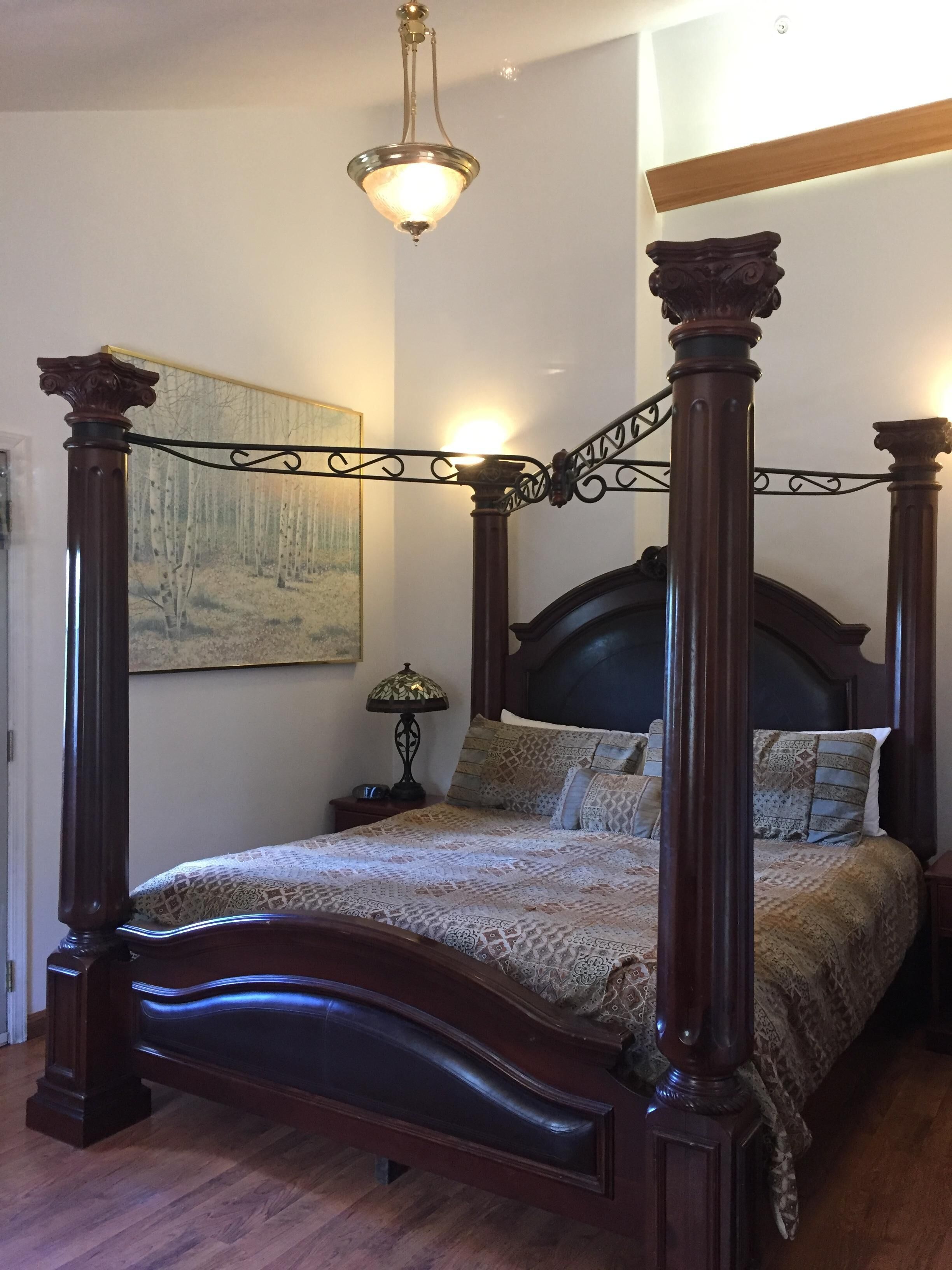 Un lit à baldaquin avec une structure en bois foncé et une couvre-lit à motifs. Une table de chevet avec une lampe se trouve à côté du lit.