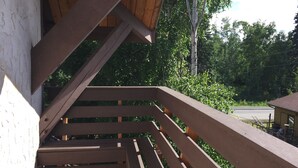 A wooden staircase leading to a covered outdoor area with a view of a road and greenery.