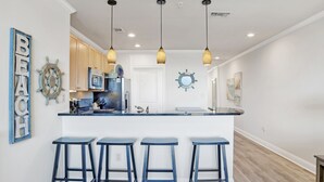 A kitchen with a central island, bar stools, pendant lights, and nautical-themed decor. - Waterfront 1BR + Bunk Alcove at The Wharf • Sleeps 6 • Amazing Views • Oasis Pool (Orange Beach)