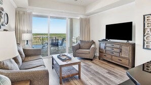 A spacious living room with a large flat-screen TV, a ceiling fan, and a view of the outdoors through a sliding glass door. - Waterfront 1BR + Bunk Alcove at The Wharf • Sleeps 6 • Amazing Views • Oasis Pool (Orange Beach)