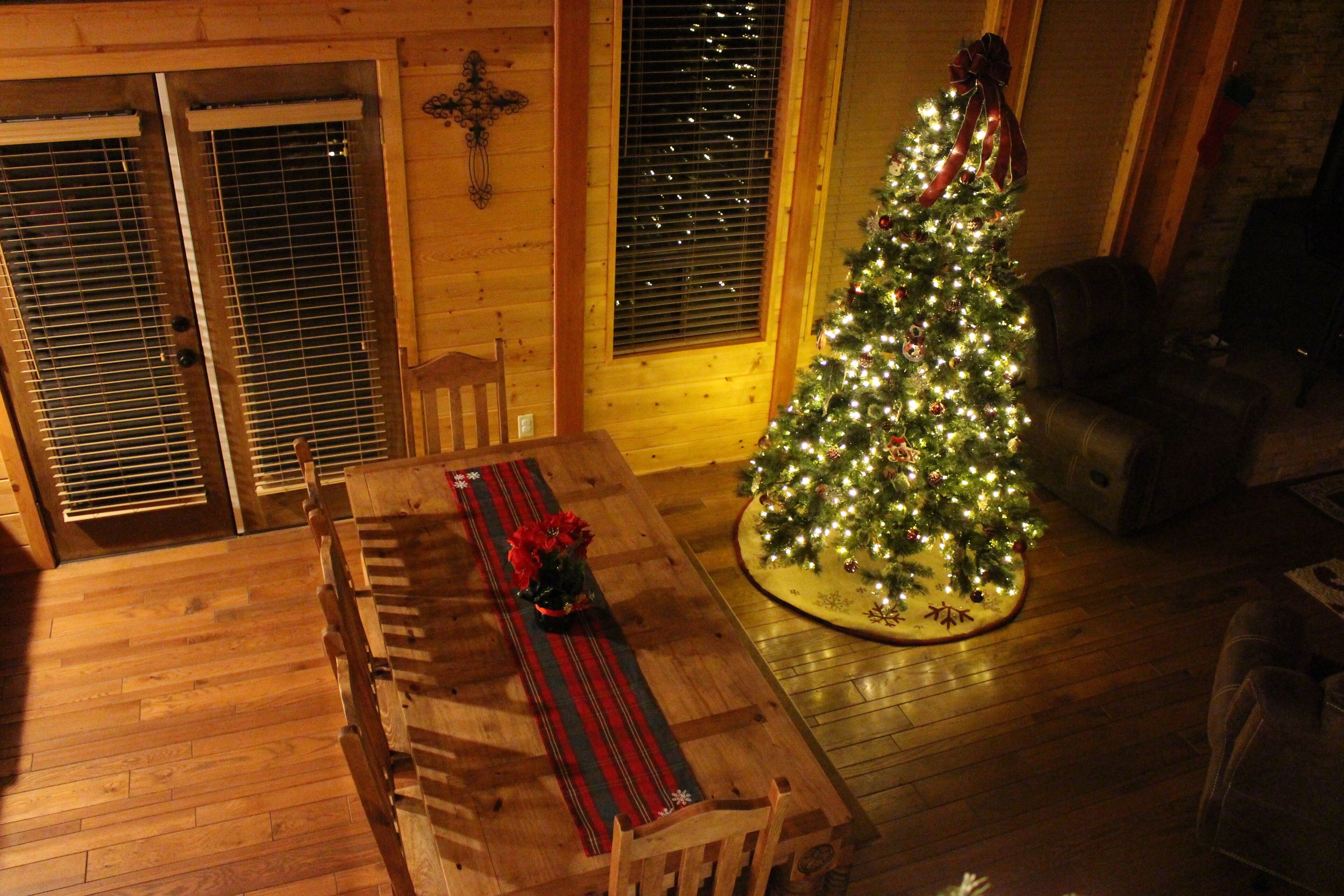 Un tavolo da pranzo in legno con un sottopiatti a righe rosse e nere, un albero di Natale con luci e decorazioni, e una panca in legno.