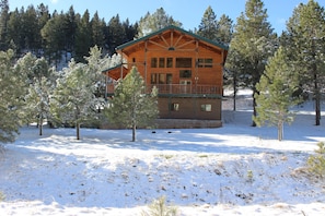 Uma cabana de madeira com varanda, rodeada por árvores cobertas de neve.