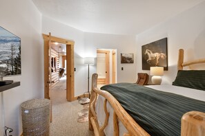 Una camera da letto con una testiera in legno, un letto con copriletto verde, un quadro appeso, una lampada e vista su un paesaggio innevato attraverso una finestra.
