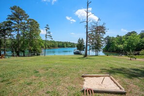 A grassy area with a wooden deck and a rope, overlooking a lake with a dock and a gazebo.