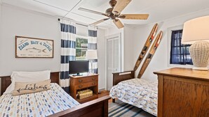 A bedroom with two beds, a ceiling fan, a framed sign, and a window with curtains.