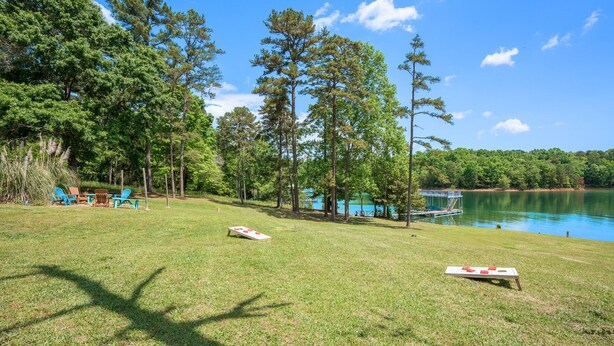 A grassy area with a dock and a small boat, surrounded by trees and a clear blue sky.