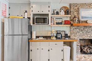 Cozinha compacta com geladeira, micro-ondas e lareira de pedra.