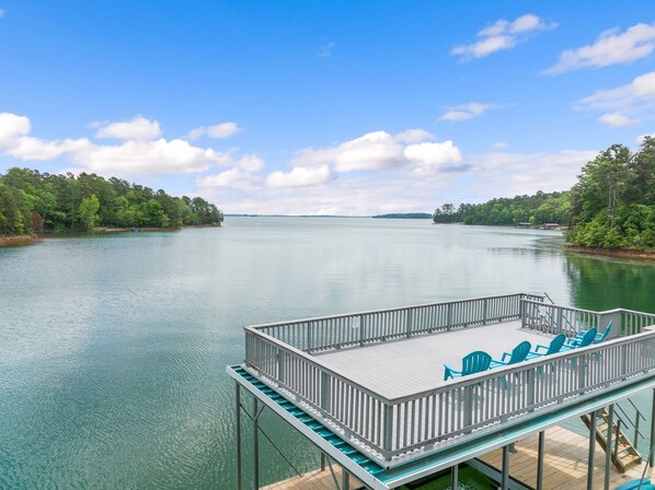A dock with chairs and a railing overlooking a calm lake with trees on the banks.