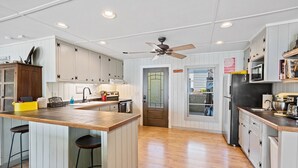 A spacious kitchen with wooden countertops, white cabinets, a central island with stools, a ceiling fan, and a view of the backyard through a glass door.