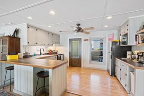 A spacious kitchen with wooden countertops, white cabinets, a central island with stools, a ceiling fan, and a view of the backyard through a glass door.