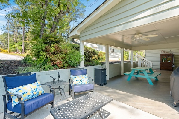 A covered patio with outdoor seating, a ceiling fan, and a view of the surrounding greenery.