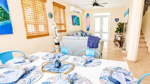 A dining area with a table set for four, a sofa, and a staircase leading to another room. - Surfing Privacy and Relaxation!  Wi-Fi, full A/C! (Rincon)