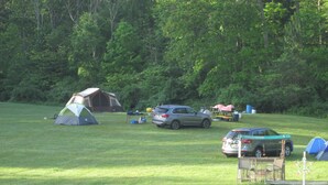 Un terrain de camping avec des tentes, une voiture et une table de pique-nique.