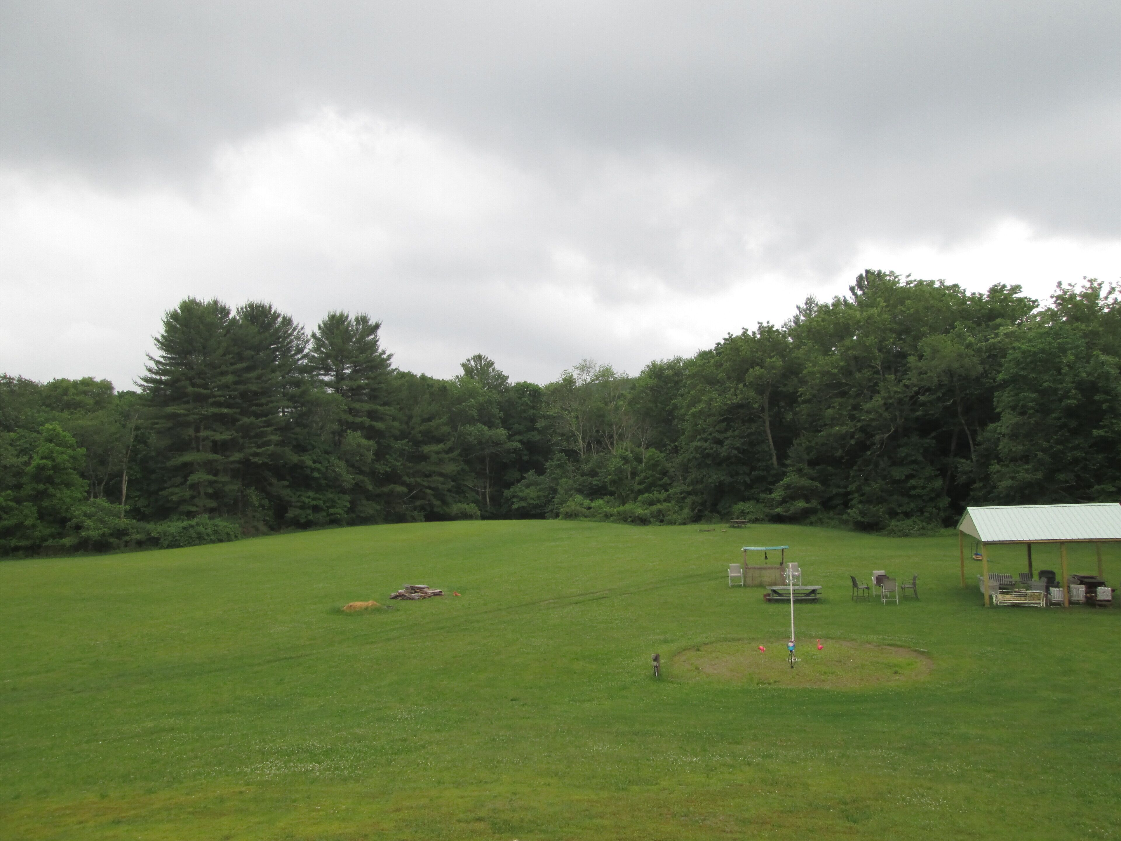 A large open grassy field with a small pavilion and picnic tables.