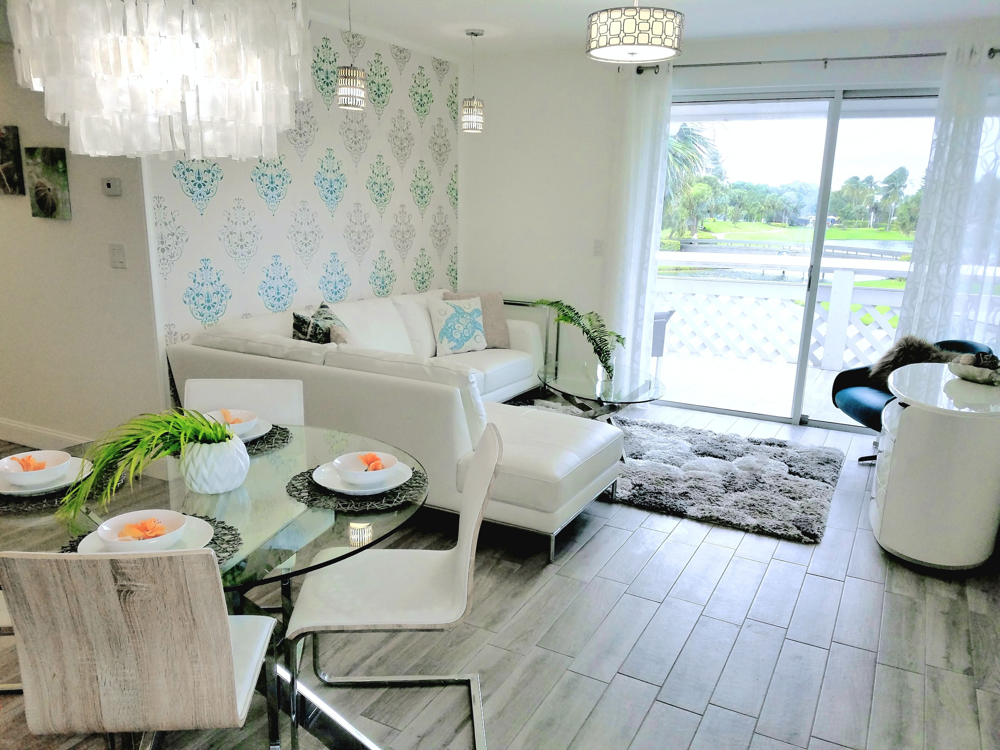 Un salón moderno con una mesa de comedor de cristal, sofás blancos y vistas a un jardín a través de un ventanal corredero.