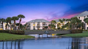 A hotel with a bridge over a calm water body, surrounded by palm trees and well-maintained lawns. - POSHPADZ -Villa Koalua Walk to Jupiter Beach-Prime Lake Views-Resort Setting (Jupiter)