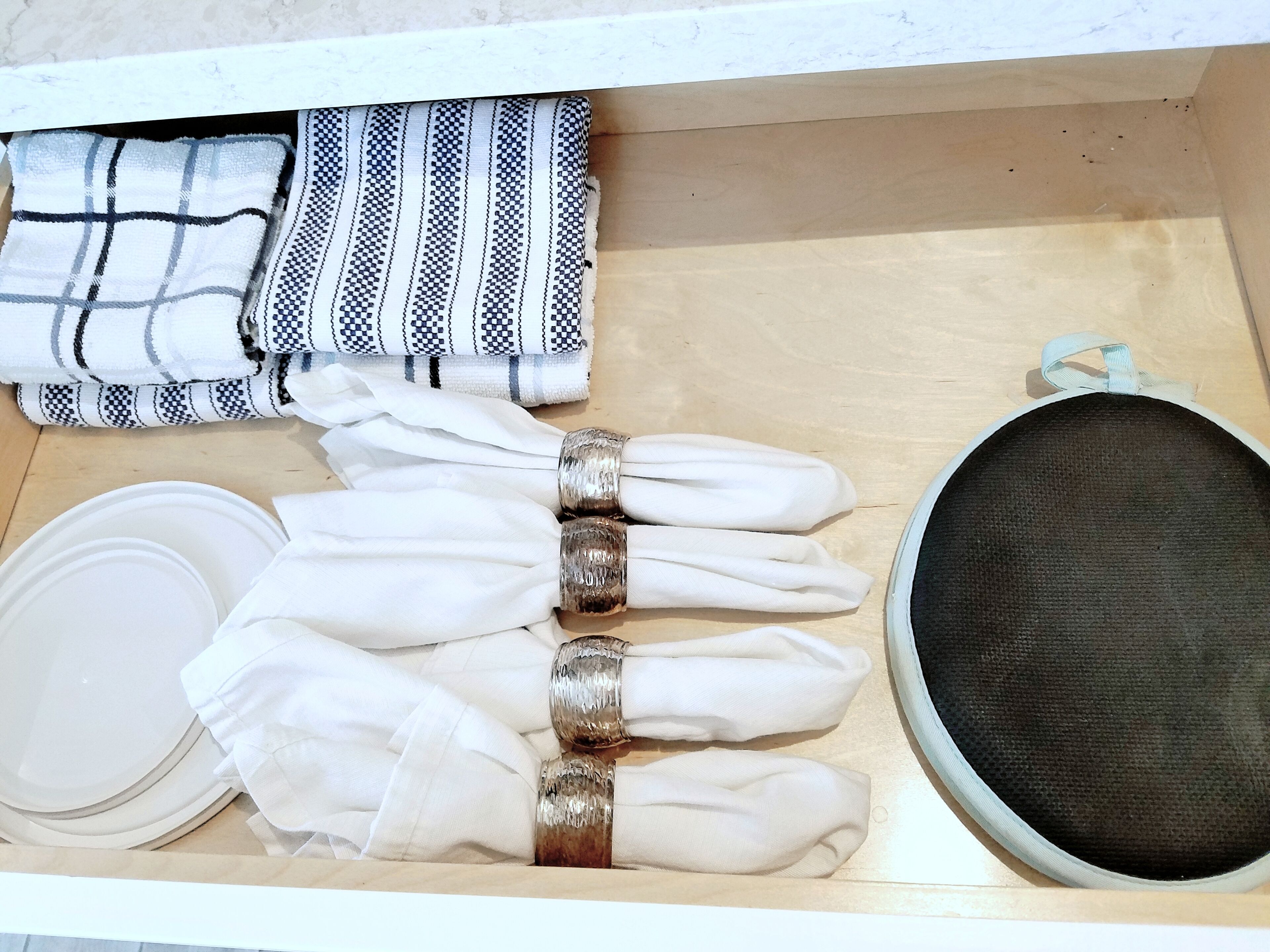Uma gaveta com guardanapos brancos dobrados, um pano quadriculado preto e branco e uma tigela de malha preta.