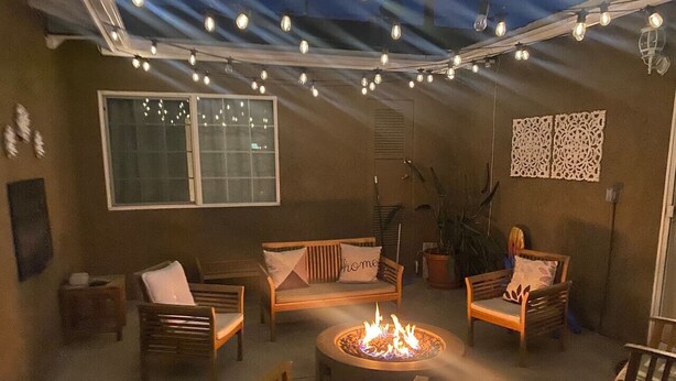 Un área de estar exterior acogedora con una chimenea, luces colgantes y un ventanal grande.