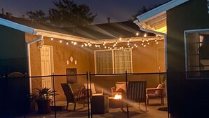 Un área junto a la piscina con un porche cubierto, mobiliario exterior e iluminación con guirnaldas de luces.