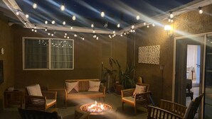 Un patio al aire libre con luces colgantes, una chimenea y zonas de estar.