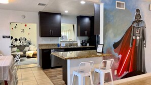 Una cocina moderna con armarios oscuros, encimera de granito y un mural del personaje Darth Vader.