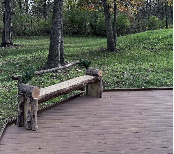 Een houten bank met een natuurlijke boomstam rugleuning op een houten terras in een park.