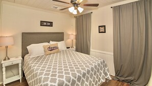 A bedroom with a patterned bedspread, a ceiling fan, a nightstand with a lamp, and a framed sign on the wall. - Howdy Headquarters~ A Backyard Gathering Like no Other! (College Station)