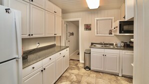 A kitchen with white cabinets, a granite countertop, a microwave, and a sink. - Howdy Headquarters~ A Backyard Gathering Like no Other! (College Station)