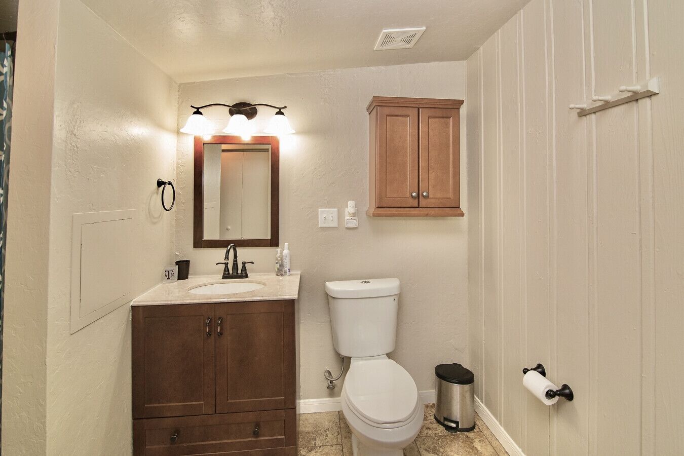 Un bagno con il water bianco, un mobile bagno in legno con specchio e luci, e un armadietto sopra il water.