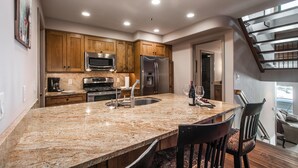 A kitchen with granite countertops, wooden cabinets, stainless steel appliances, and a central island with seating. - Wonderful Park City Townhome | Hot Tub | Mountain Views | Private Garage (Park City)