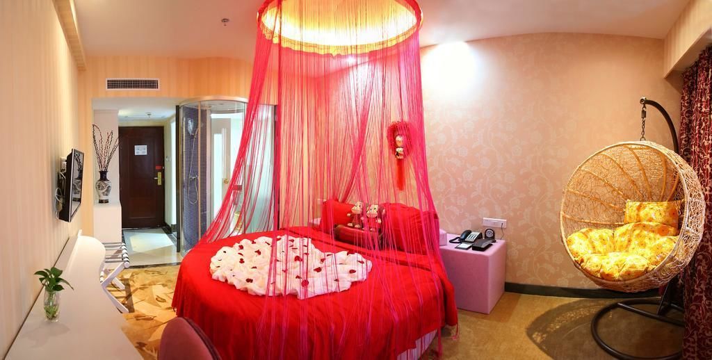 A hotel room with a large bed, a hanging chair, and a bedside table with a lamp.