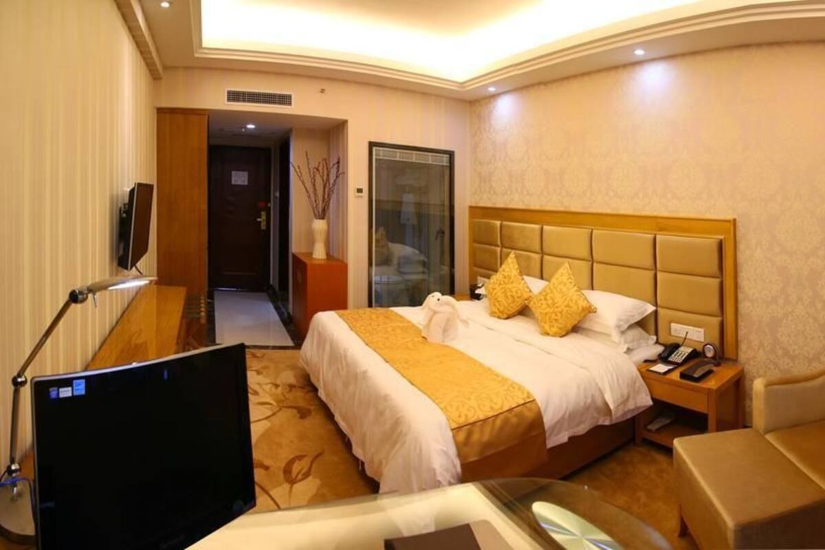 Une chambre d’hôtel avec un grand lit, un bureau avec un ordinateur, une chaise et une petite table sur laquelle est posée une plante.