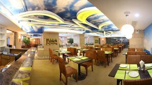 A restaurant with a modern interior, featuring a ceiling with a cloud design and ambient lighting. Tables are set with green placemats and white tableware. - Xiamen Plaza Hotel (Xiamen)