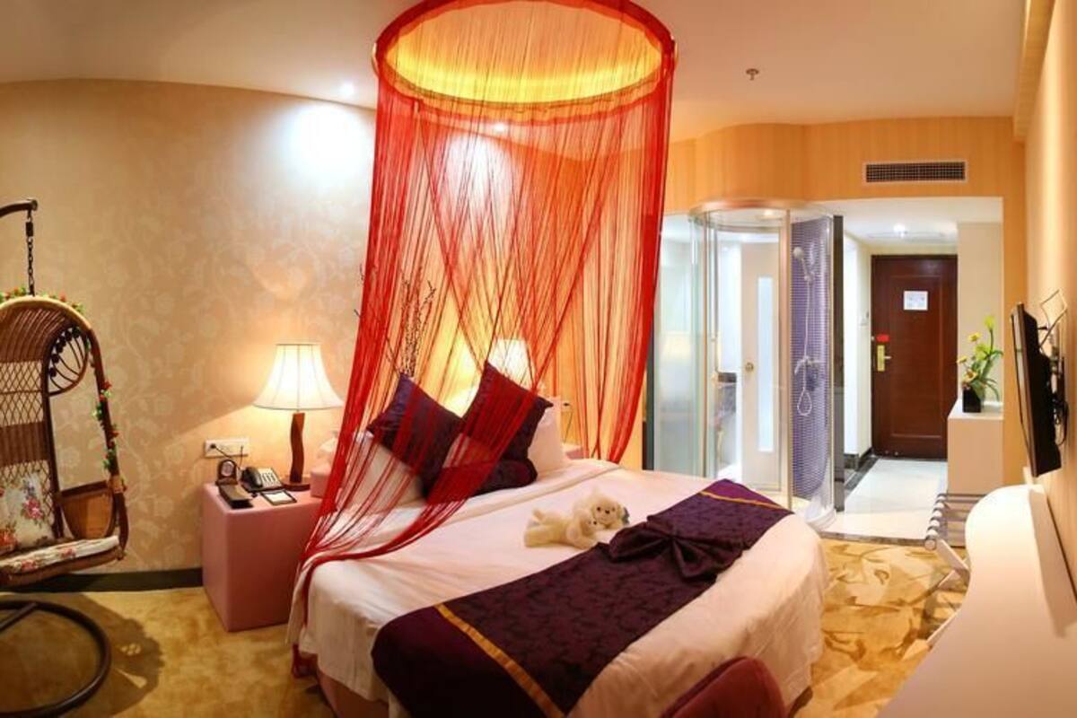 Une chambre d’hôtel comprenant un lit, une table de chevet, une chaise, une cabine de douche en verre et une porte donnant sur une autre pièce.
