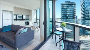 A modern apartment with a balcony, a sofa, a dining table, and a kitchen area. - Wyndel Apartments Riverside on Collins (Docklands)
