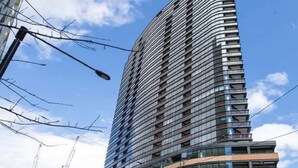 A modern high-rise building with multiple floors, large windows, and a curved facade. - Wyndel Apartments Riverside on Collins (Docklands)