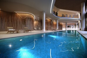 Une piscine intérieure moderne, avec une eau d’un bleu cristallin, entourée de chaises longues et dotée d’un design contemporain agrémenté d’éléments en bois et d’un éclairage aux lignes courbes.