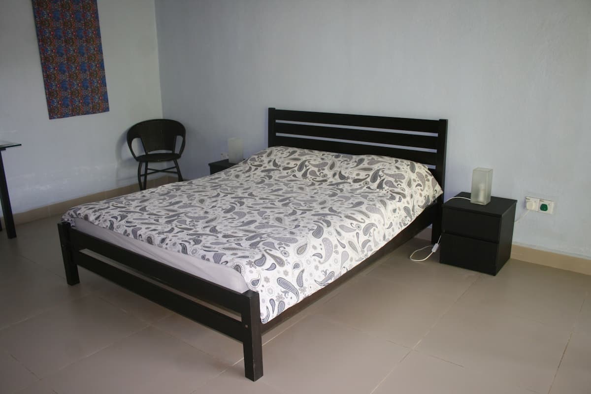 Un dormitorio con cama, una silla, una mesita de noche y una lámpara fijada a la pared.