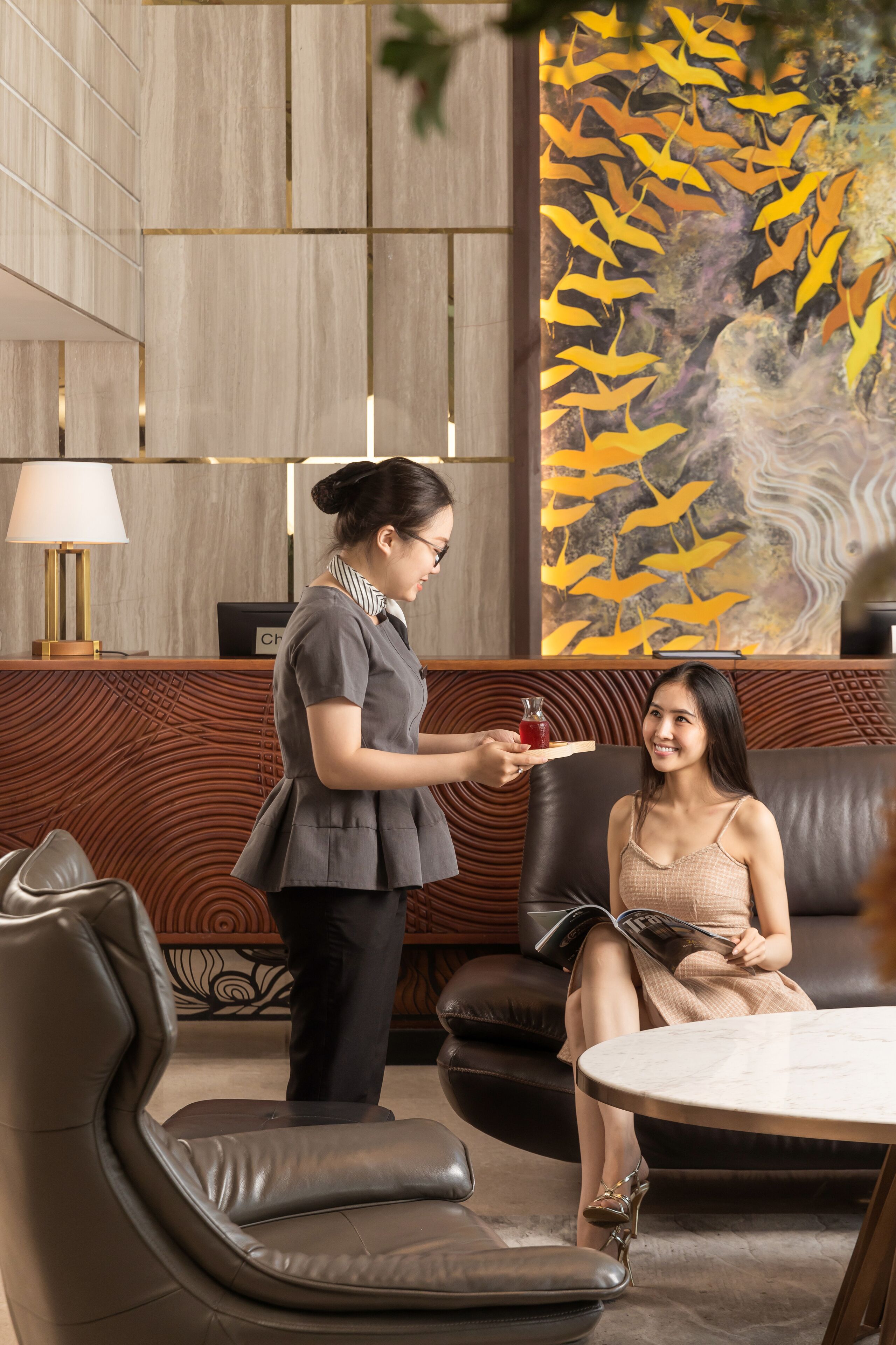 A reception area with a wooden reception desk, a modern lamp, and a wall mural of birds.