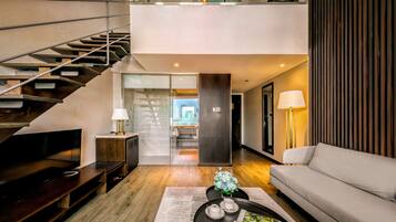 A modern living room with a staircase, a sofa, a coffee table with a magazine, and a lamp.