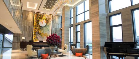 A spacious lobby with a grand piano, comfortable seating, a large decorative wall, and large windows.