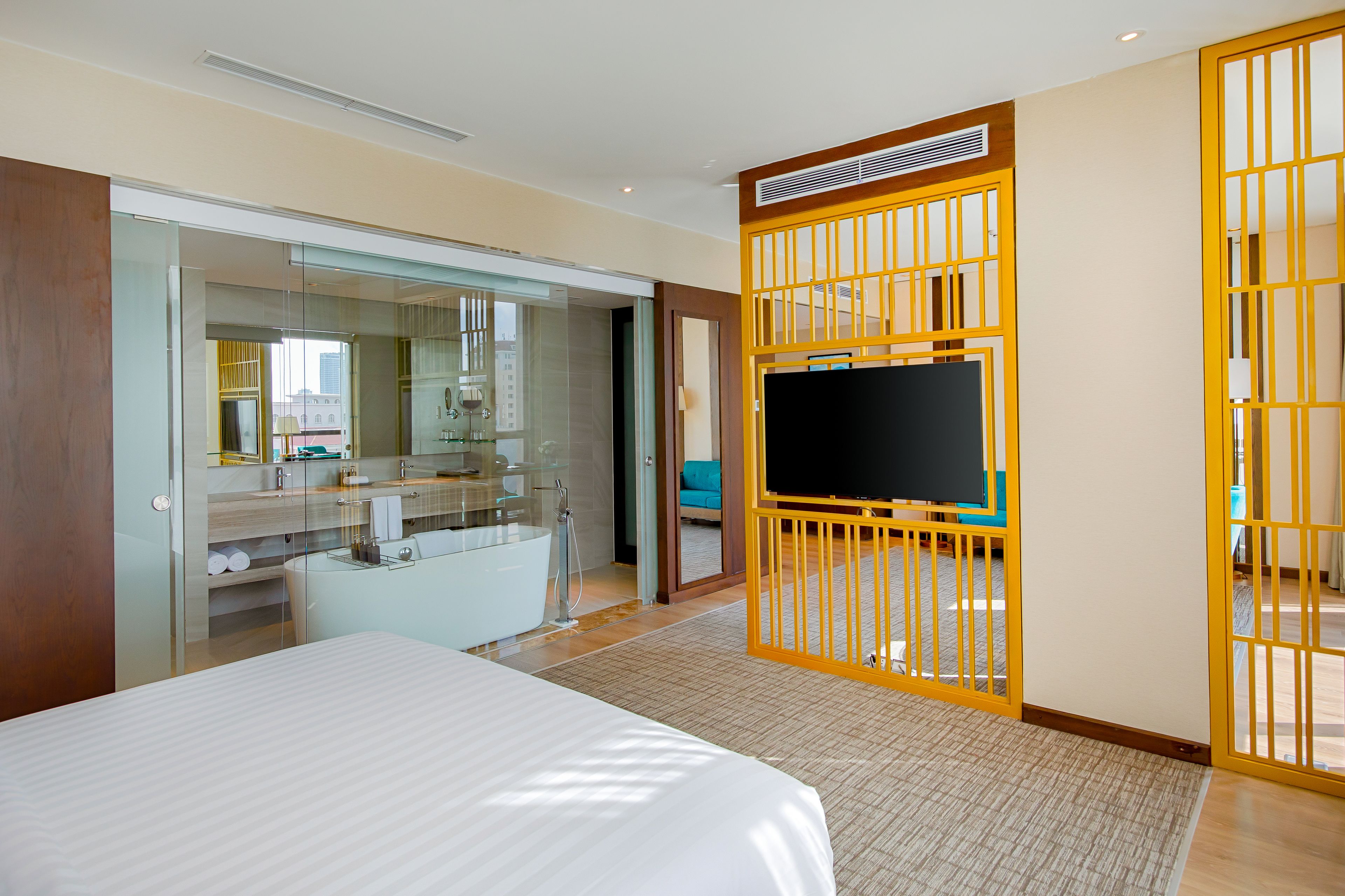 A hotel room with a bed, a TV, a bathroom with a bathtub, and a sliding glass door to a balcony.