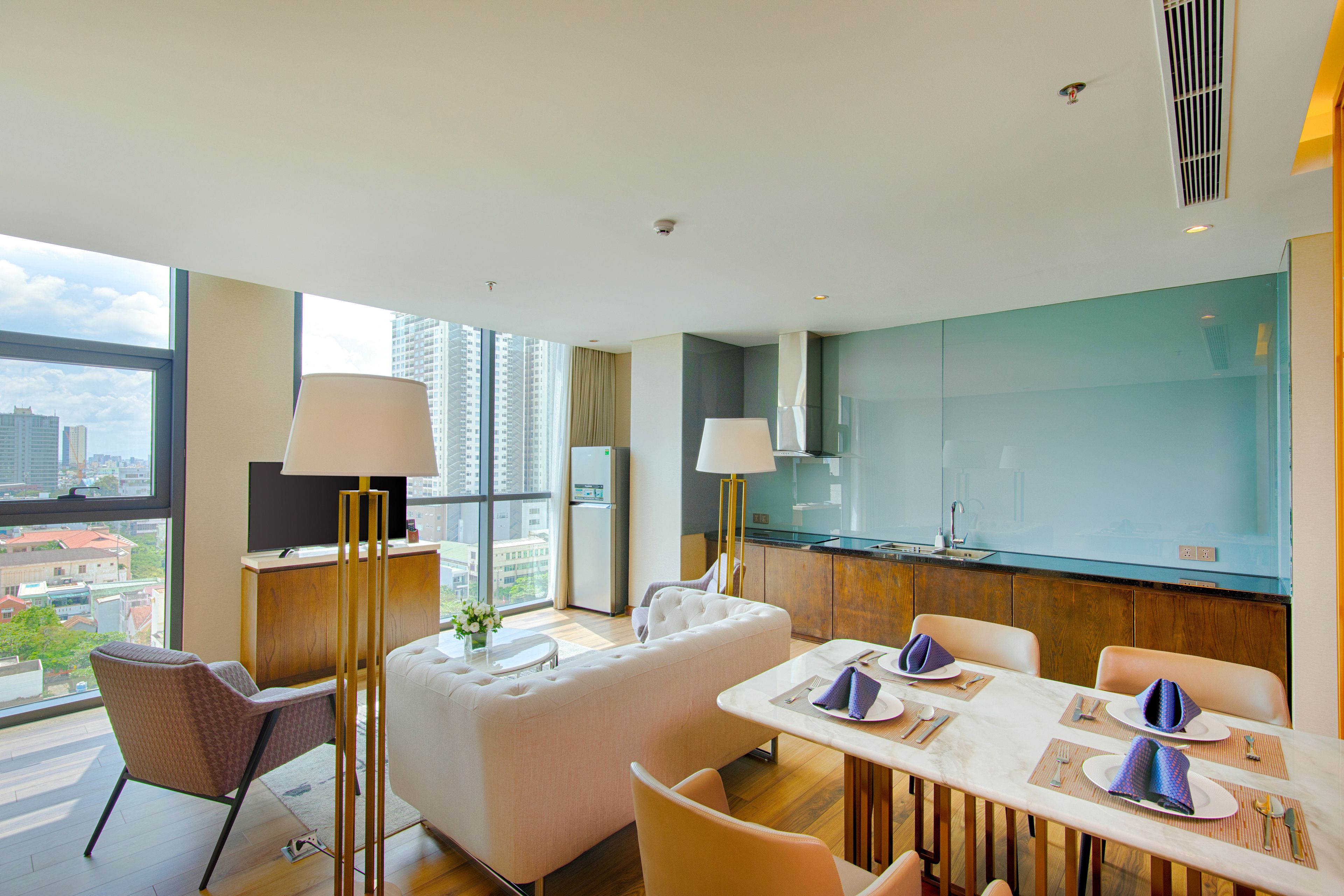 Una habitación de hotel moderna con un gran ventanal, un sofá, una mesa de comedor para cuatro personas y una zona de cocina.