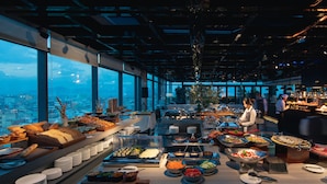 A buffet with various food items and a city view through large windows. - New Orient Hotel Danang (Da Nang)